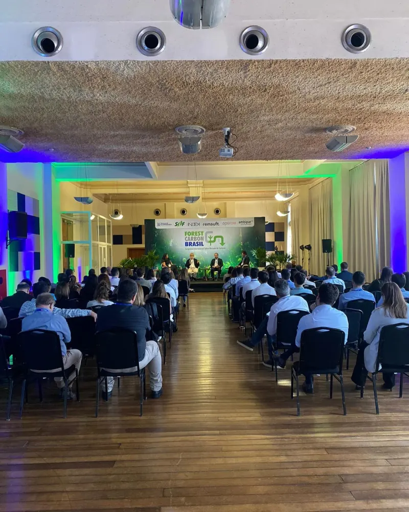 Auditório com plateia em evento corporativo, com caixas de som e iluminação verde e azul