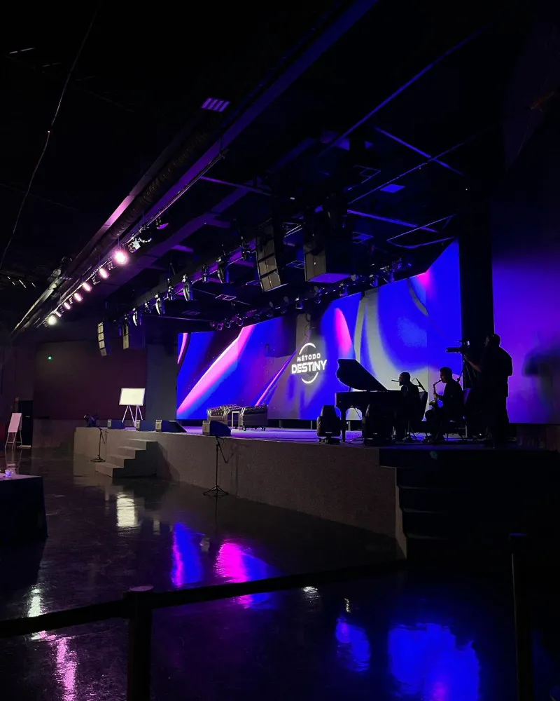 Palco com painéis de LED em tons de azul e roxo atrás da banda, com piano à esquerda