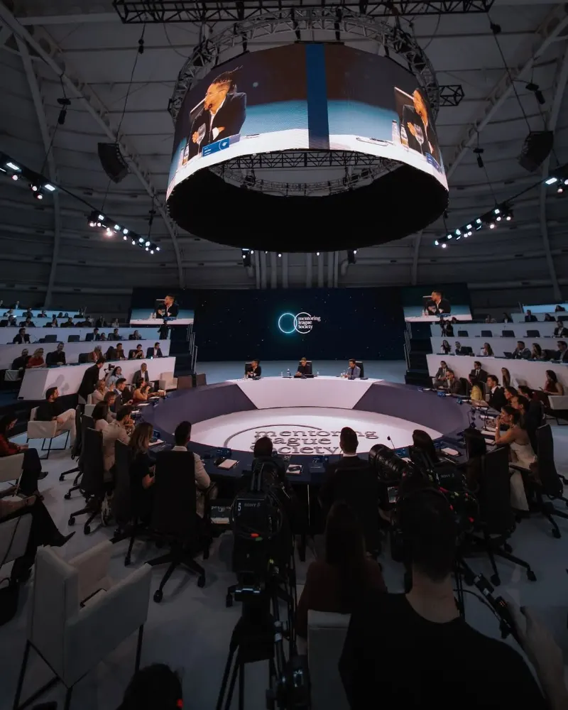 Palco circular no centro de uma arena com telão suspenso e plateia em volta