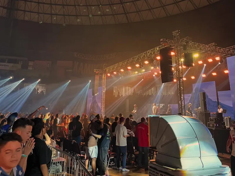 Show em arena lotada com line array pendurado na treliça e feixes de luz sobre o palco